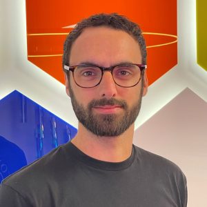 A friendly man with glasses standing in front of a colourful background.