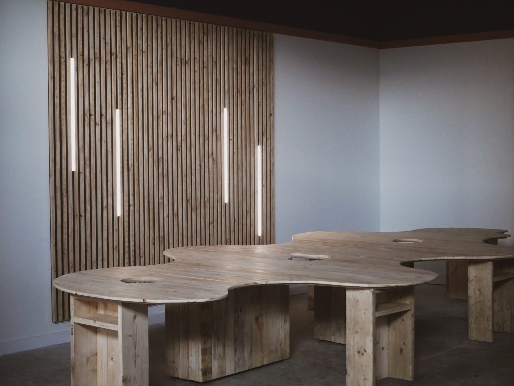 Bespoke six-person office workstation made from reclaimed timber beside a slatted wood feature wall with integrated lighting.